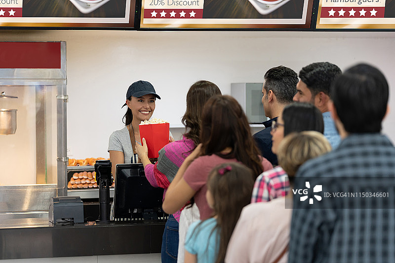 在电影院特许摊位卖食物的快乐女人图片素材