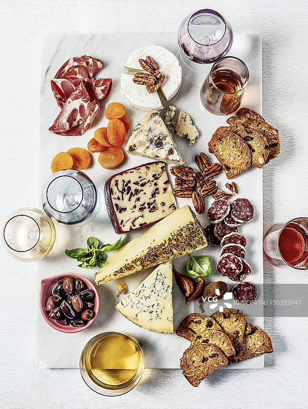 奶酪拼盘：搭配核桃、干果、萨拉米和意式火腿的法国奶酪，置于白色背景的大理石砧板上图片素材