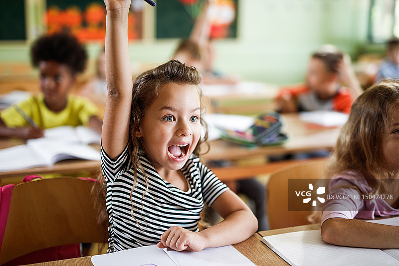 快乐的小学女生在课堂上举手回答问题图片素材