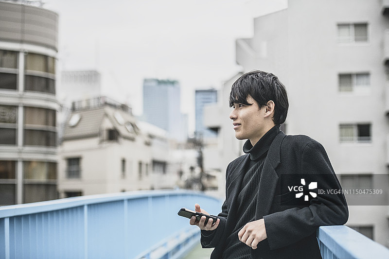 手持手机的英俊日本青年男子的人物画像图片素材