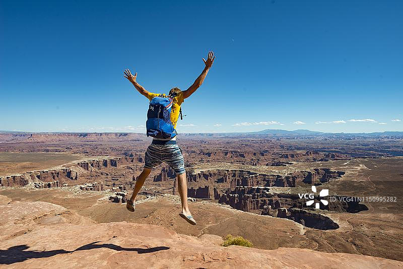 在峡谷地国家公园绿色河流大观景点张开双臂跳跃的年轻男人图片素材