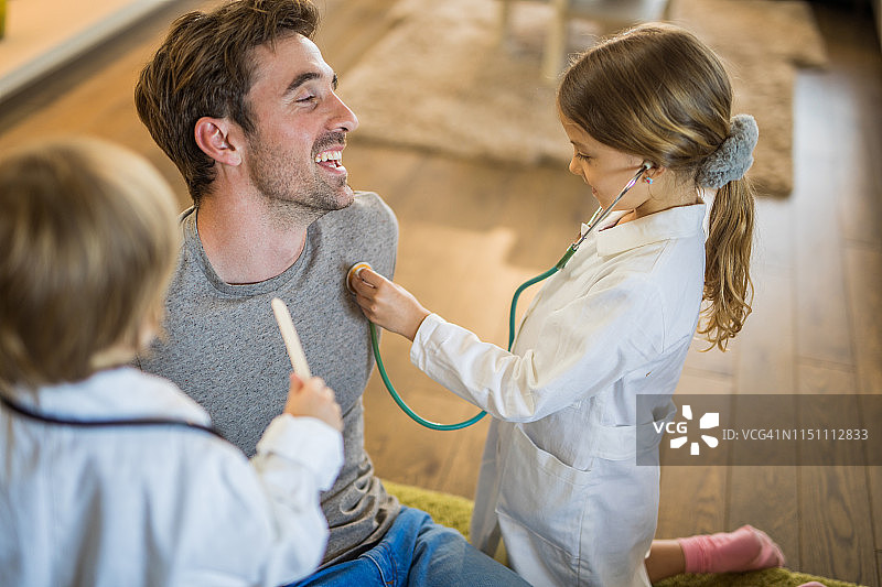 孩子们假装是医生，在家里检查他们的父亲图片素材