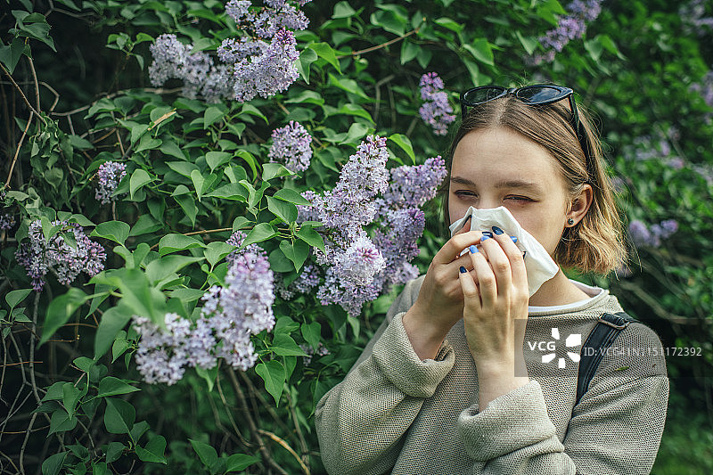 春天公园里因花粉过敏打喷嚏，正在擦鼻子的女孩图片素材