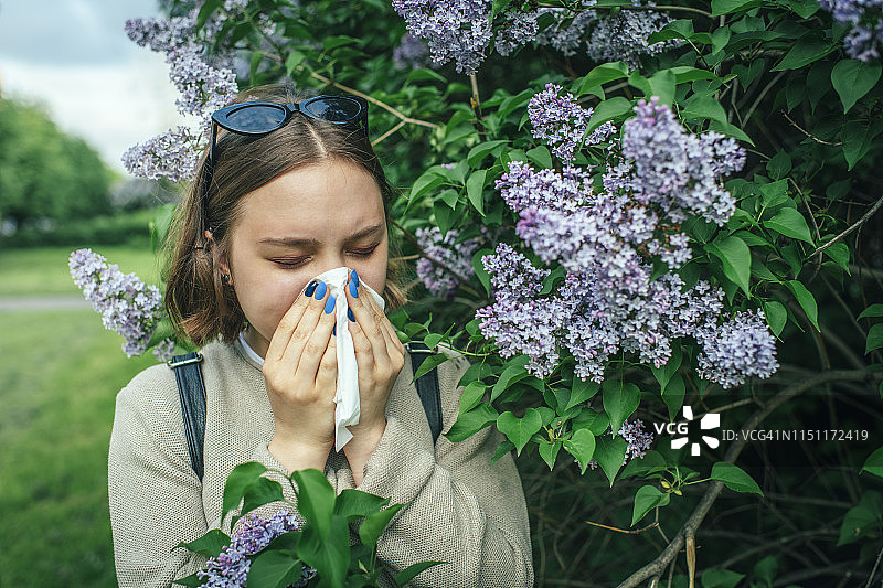 春天公园里因花粉过敏打喷嚏，正在擦鼻子的女孩图片素材