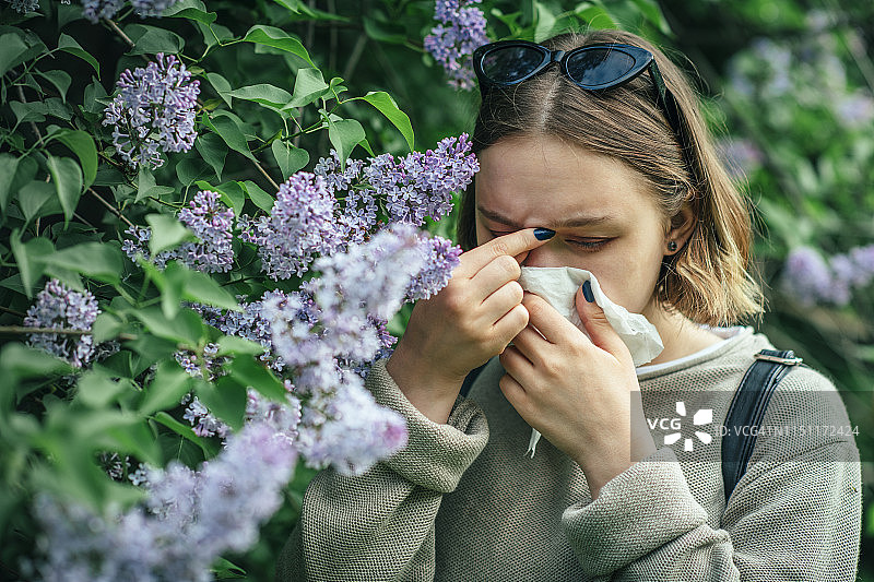 春天公园里因花粉过敏打喷嚏，正在擦鼻子的女孩图片素材
