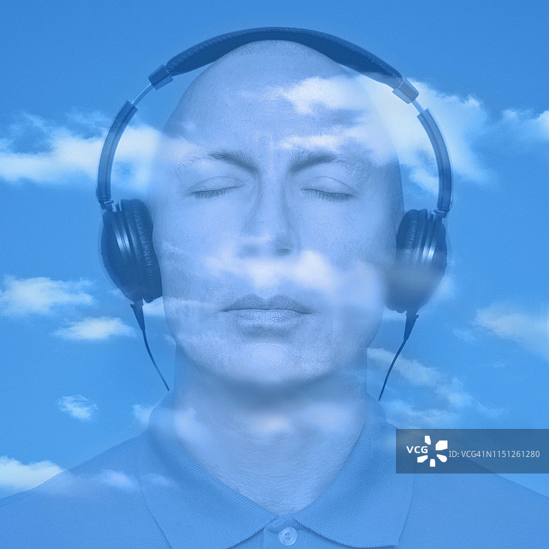戴着耳机，头顶是蓝色天空和云彩的男子肖像图片素材