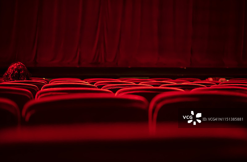 红发女子坐在空旷剧院的红色天鹅绒座位上图片素材
