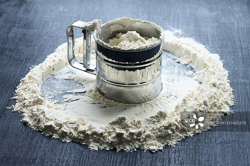 面粉筛子装满面粉，散落在深色木质背景上图片素材