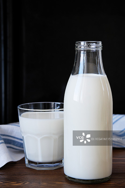 玻璃瓶装鲜牛奶与木桌上的牛奶杯，搭配亚麻条纹毛巾图片素材