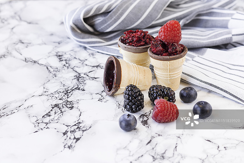 野生浆果冰淇淋，配新鲜野生浆果和条纹餐巾，在冰淇淋甜筒中。白色大理石背景桌面上的配料。选择性聚焦和复制空间图片素材