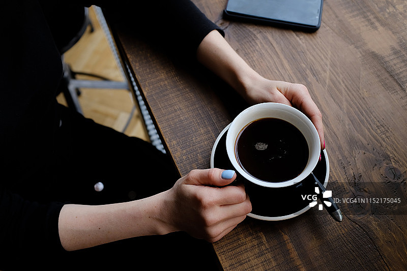 女孩在咖啡馆的木桌旁手捧咖啡，电话在侧图片素材