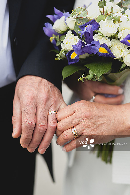 在教堂婚礼后，一对年长的夫妇手部特写。年长的夫妇结婚，新娘手捧着一束美丽的白色和紫色鲜花图片素材