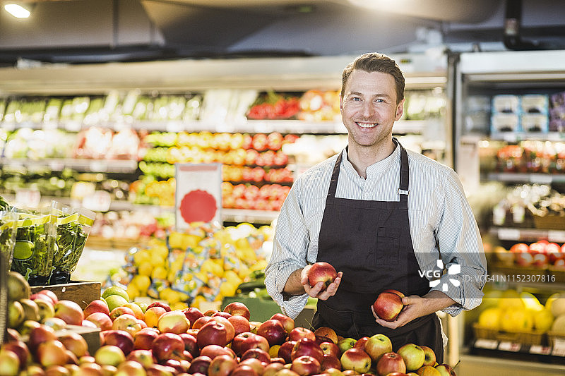 杂货店苹果摊位前微笑的中年店主肖像图片素材