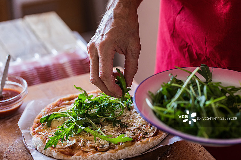 制作披萨，顶部撒上新鲜芝麻菜叶图片素材