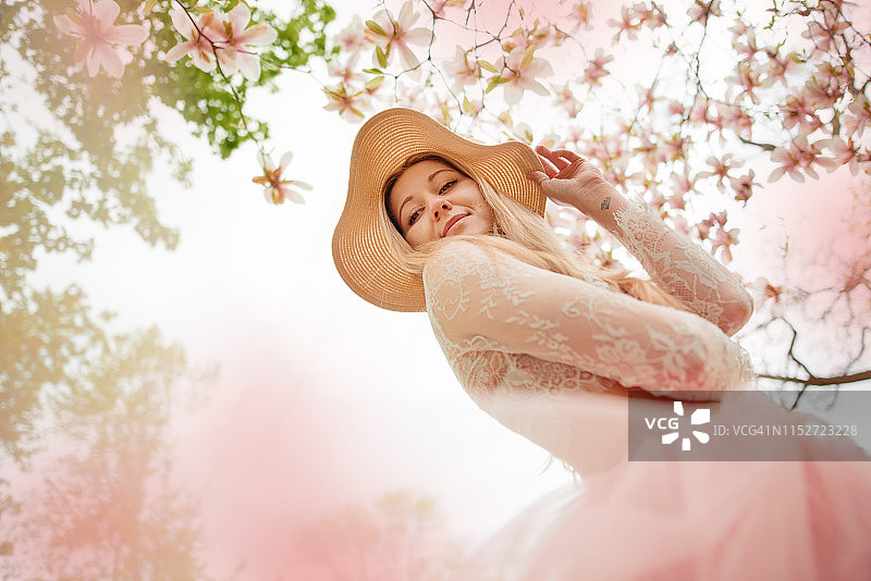 穿着珊瑚色裙子的女人在鲜花盛开的公园里欣赏美景图片素材