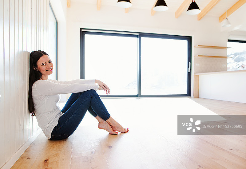 坐在新家空荡客厅地板上的年轻女人，看着镜头图片素材