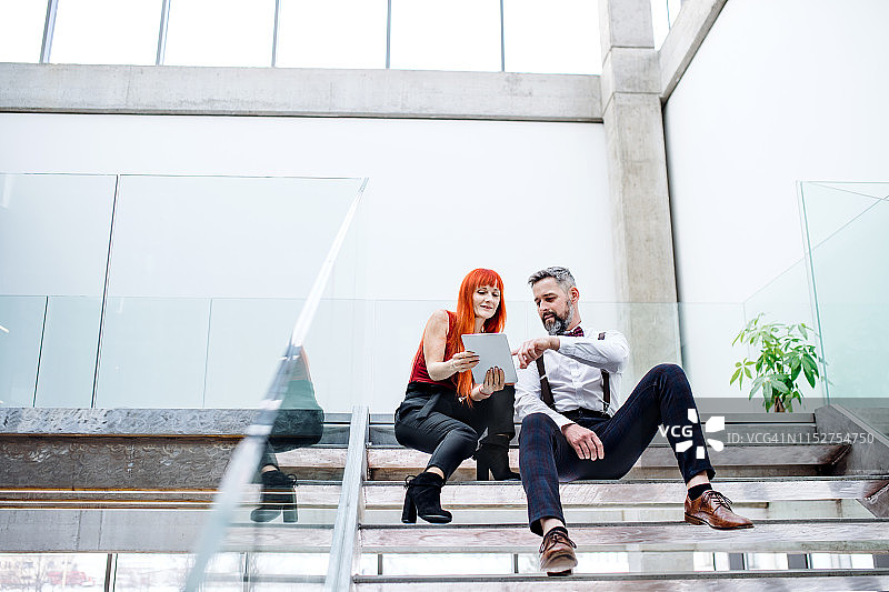 两位商人坐在楼梯上用平板电脑讨论问题图片素材