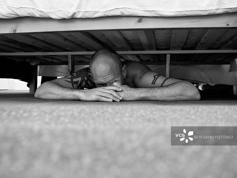 男人捂着眼睛躲在床下图片素材