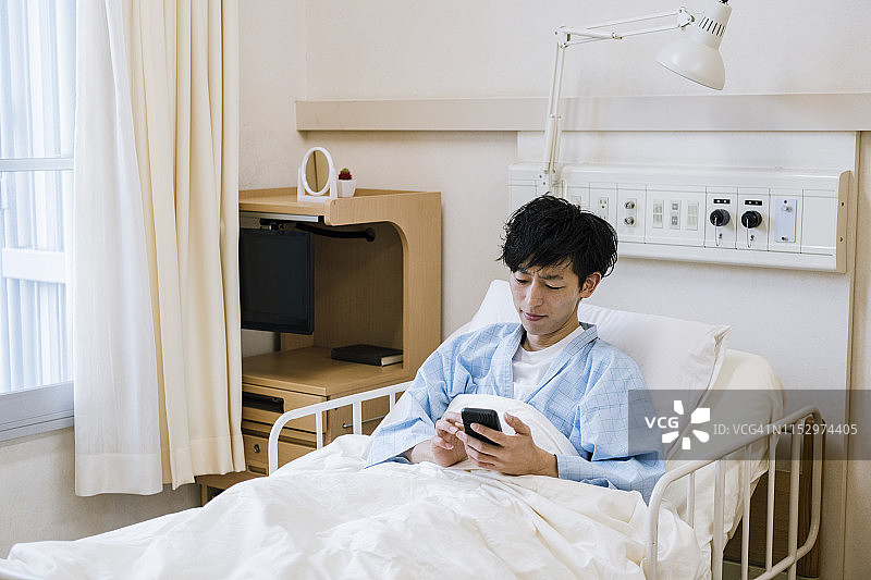 在医院病床上发短信的中年男人图片素材
