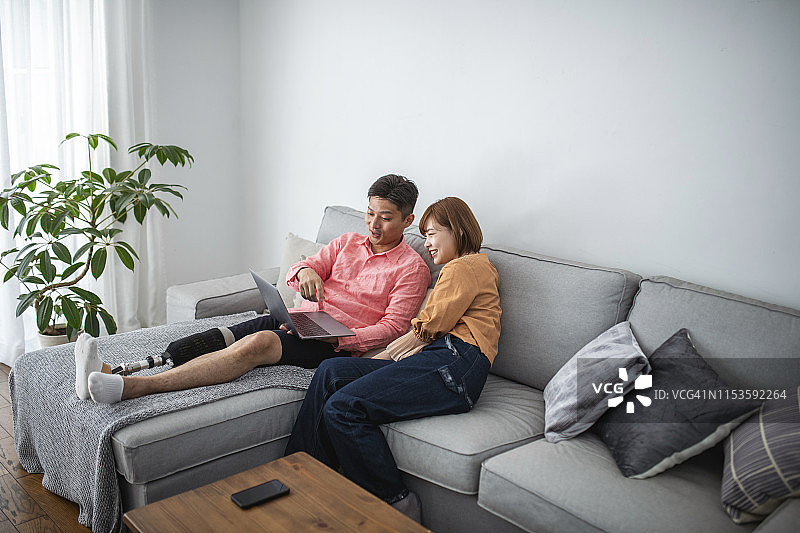 残疾日本男子与妻子在沙发上用笔记本电脑放松图片素材