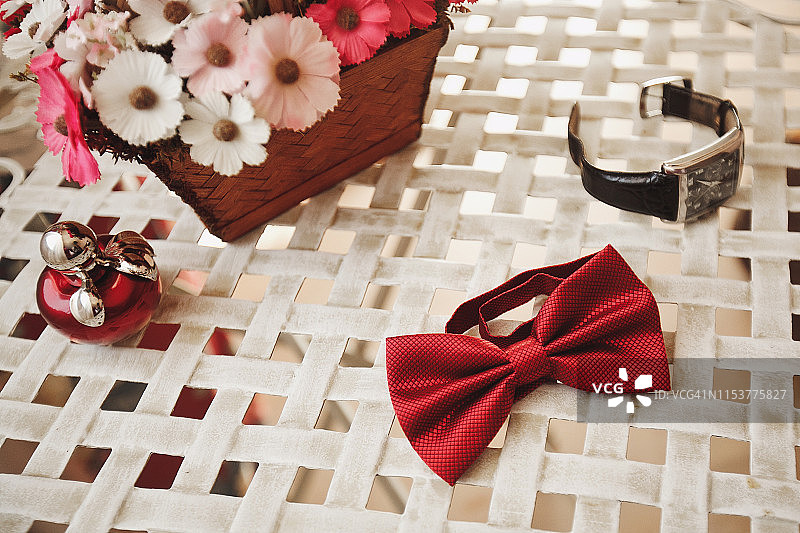 婚礼配饰：咖啡桌上的女士香水、装饰花篮、男士红色领结和手表，新娘新郎的婚礼准备图片素材