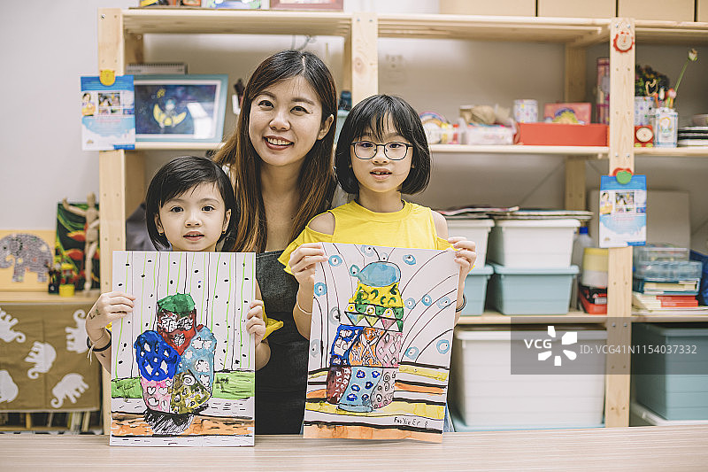 在艺术中心上课后展示绘画作品的亚洲华人儿童与他们的美术老师看着镜头图片素材