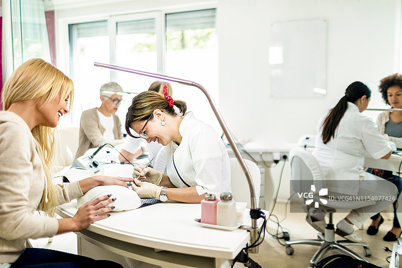 美甲师在美容院为金发女人修剪指甲角质层图片素材