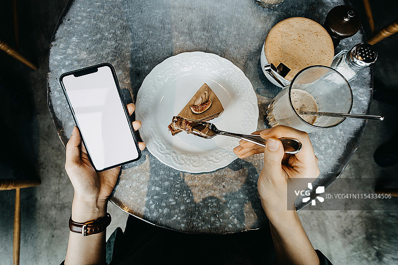 俯视角度：在咖啡馆享受咖啡和蛋糕时使用智能手机的女人图片素材