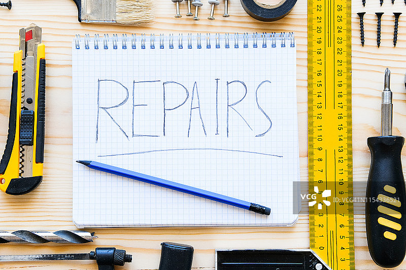 木桌上带有“修理”字样的笔记本、一杯茶和用于建造房屋或公寓修理的工具，工长的的工作场所，家庭和专业维修、建筑的主题图片素材