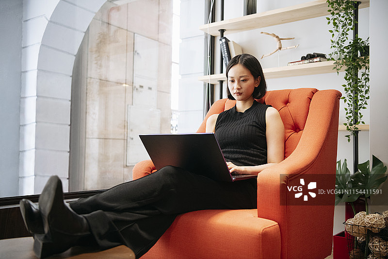 亚洲女性坐在橙色大椅子上使用笔记本电脑图片素材
