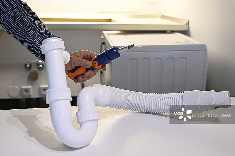 男人手持螺丝刀修理厨房水管连接处，居家管道维修图片素材