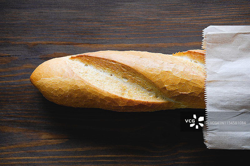 装在纸袋里的新鲜面包，在棕色木桌的砧板上，特写，有机农产品理念图片素材