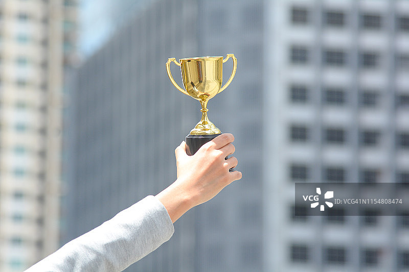 手握奖杯，城市建筑背景，象征商业成功图片素材