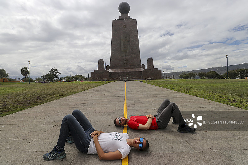 在厄瓜多尔世界赤道纪念碑，两人躺在分隔两个半球的黄线上图片素材