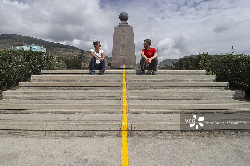 两人坐在厄瓜多尔世界之半纪念碑的黄线上图片素材