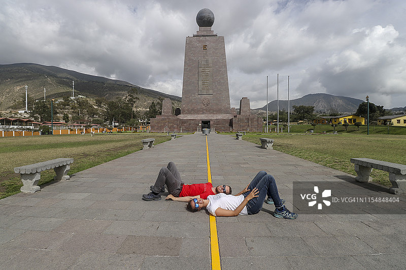 在厄瓜多尔世界赤道纪念碑，两人躺在分隔两个半球的黄线上图片素材