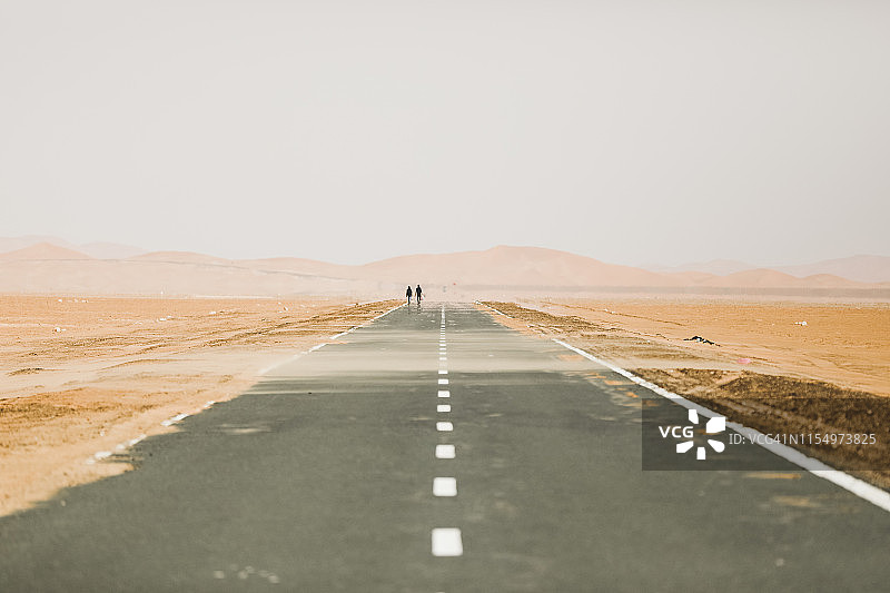 沙漠中道路上行走的两个人图片素材