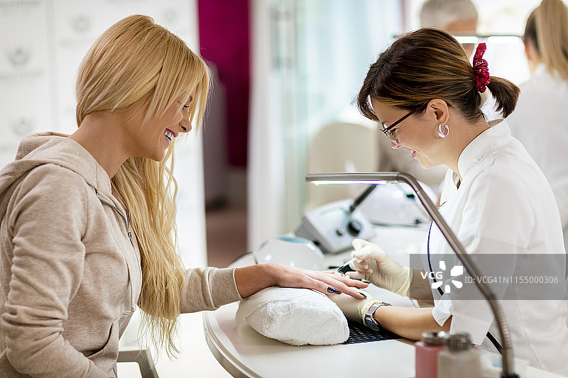 美甲师在美容院为金发女性涂指甲油图片素材