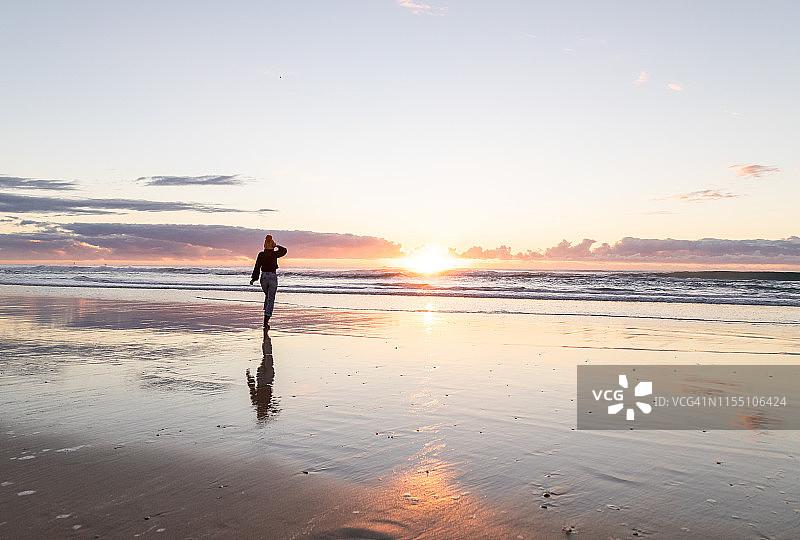 穿着冬装的年轻亚洲女士在日出时走在沙滩上图片素材