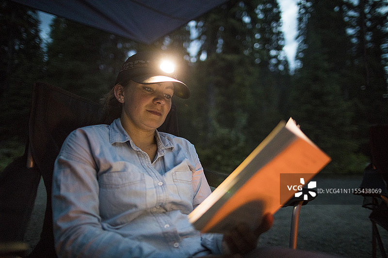 戴着头灯在户外露营时看书的女人图片素材