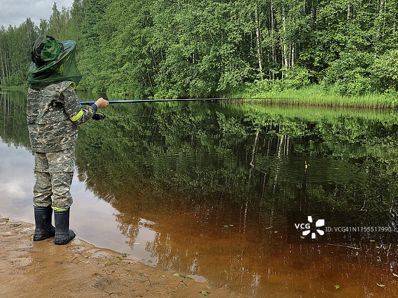 孩子在森林河流附近穿着防护服钓鱼，防止蚊虫叮咬图片素材