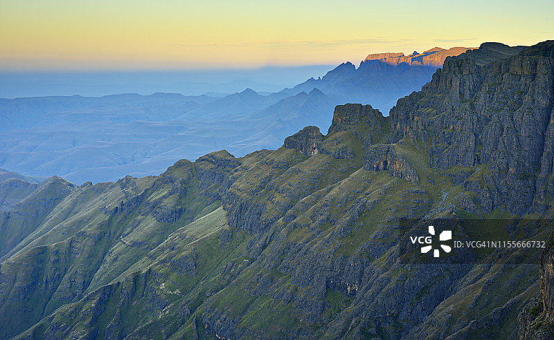 阳光照射在远处的山顶上，前景是饱经沧桑的山坡，南非夸祖鲁-纳塔尔省德拉肯斯堡大教堂山脉图片素材