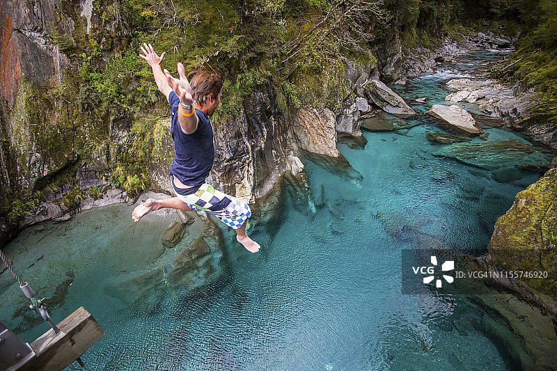 马卡罗拉的蓝色水池：诱人的蓝色水域，一名男子从桥上跳入水中图片素材