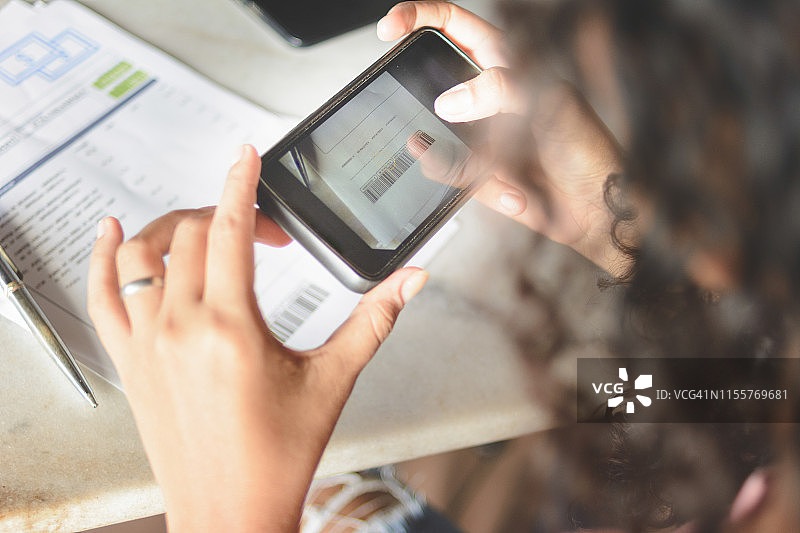 用智能手机拍摄条形码，通过网上银行应用程序支付账单的女人图片素材