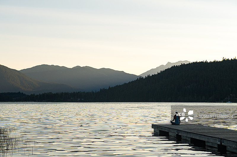 女人在山间湖泊的码头上冥想图片素材