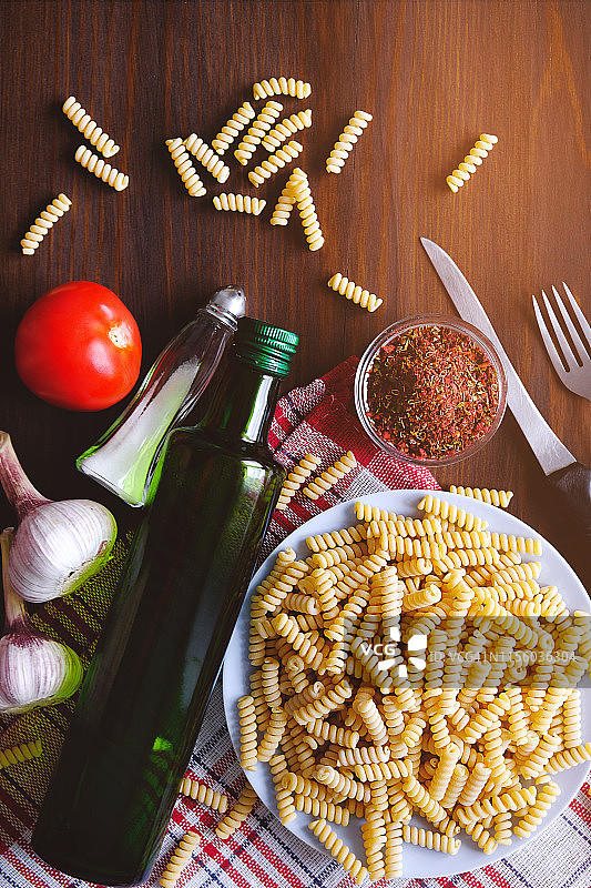 意大利面、橄榄油、香料、西红柿、盐、大蒜、刀叉摆放在深色木桌上。顶部视角，留有文案空间。意大利美食概念。烹饪素食或纯素食品。图片素材