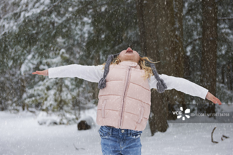 冬天，年轻女孩站在森林小路上，用舌头接住雪花图片素材