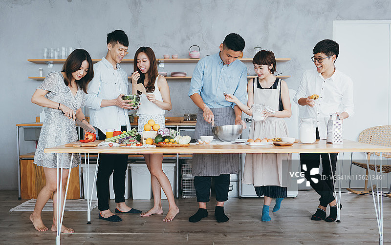 快乐的亚洲年轻男人和女人在现代厨房一起做饭，一边聊天一边为聚会准备食物图片素材