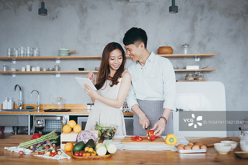年轻夫妇在厨房做饭时查看平板电脑上的食谱图片素材