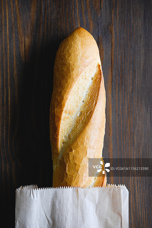 装在纸袋里的新鲜面包，在棕色木桌的砧板上，特写，有机农产品理念图片素材